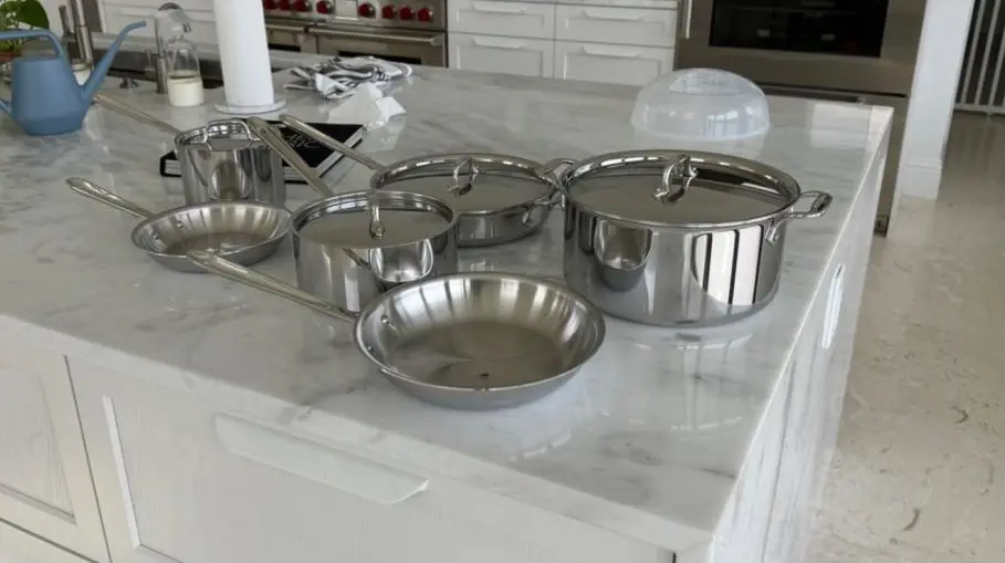 shown is an image of All-Clad D3 3-Ply Stainless Steel Cookware Set being reviewed, Fry Pans, Saucepans, Saute Pans, Stockpot, Lids, Pots and Pans on top of a kitchen table